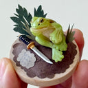 Small round wooden base with a green frog, sword, and leaves on a white background