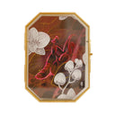 Painting on octogonal paper of a dark red orchid mantis with a hot pink outline. It sits on dark red leaves with white orchids blooming nearby. 