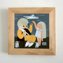 A framed whimsical illustration of two stylized figures with large beige hairdos, one seated in a black outfit and one standing in a white dress, set against a dark blue-gray background. The artwork is housed in a light natural wood frame and mounted on a white wall.