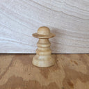 A small handcrafted wooden object with a rounded dome top and flared base, shown standing on a wooden surface against a light wood background.