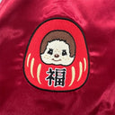 Embroidered patch of a cartoon character in a red Daruma doll on a red fabric background
