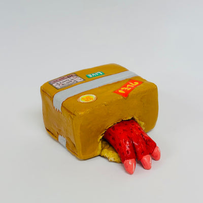 Clay sculpture of a taped up brown cardboard box, with a hole on the side where a red monster hand pokes out.