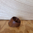 A small handcrafted wooden bowl with a dark brown finish and visible wood grain, resting on a light wood surface against a light wood background.