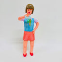 Clay sculpture of a female office worker, standing and pouring out a cup of green tea, with the green liquid halfway out. She stands with one hand on her hip.