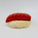 Clay sculpture of a piece of tuna nigiri sushi, with a red scored tuna atop of a rounded bed of rice.