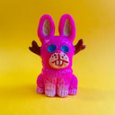 Fluorescent pink mini figurine of a rabbit, sitting with hollow blue eyes and small brown antlers coming out the side of its head, like a jackalope.