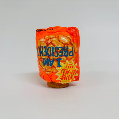 Clay sculpture of an upturned bag of chips - fluorescent orange with text that reads "I am president"