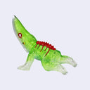 A small translucent green kaiju toy figurine with a red spiked back, a red gem on its head, and clear transparent claws and tail, shown against a light gray background.
