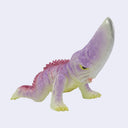 A small plastic kaiju toy figurine with a curved snout, featuring a translucent lavender-purple body, pink spikes along its back, and pale yellow feet and underbelly, set against a plain light gray background.