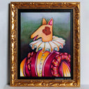 A framed whimsical painting of a dog dressed in a ruffled white collar and a pink, orange, and yellow striped outfit, set in an ornate gold frame against a light gray wall.