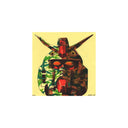 A square artwork featuring a stylized, abstract robot or mecha face in red, green, brown, and black camo pattern on a pale yellow paper, centered on a white background.
