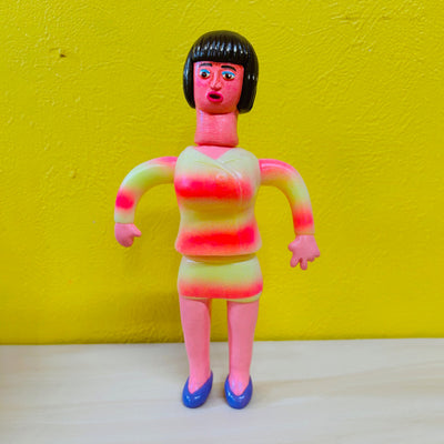 Clay sculpture of a pink woman with short black hair and bangs, wearing a matching suit top and skirt outfit - yellow to pink gradient in coloring with blue shoes.