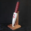 Whittled wooden sculpture of a knife, turned down and onto a stand. The blade of the knife is white with red arrow patterning and the handle is leather bound.