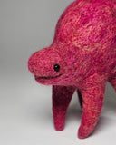 A handmade felted wool animal figurine in a vibrant magenta-pink color, standing on a neutral light gray background.