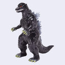 A Godzilla toy figure in a standing pose, featuring a glossy black textured body, gray back spikes, yellow-green claws and toes, and glowing red eyes, set against a plain light gray background.