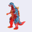 A translucent vinyl Godzilla toy figure with a red and blue color scheme and yellow flame accents on its back and claws, set against a plain light gray background.