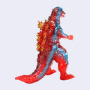 A glossy, translucent monster figurine resembling Godzilla, featuring a split red and blue color scheme with gold spikes on its back, set against a plain light gray background.
