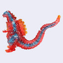 A translucent soft vinyl Godzilla figure with a red and blue color scheme and orange flame accents on its back and tail, set against a plain light gray background.