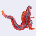 A translucent red and blue Godzilla figure with fiery orange-yellow highlights on its back and tail, shown against a plain light gray background.