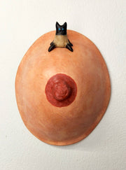 Sculpture of a single boob with a painted nipple. Sitting atop the boob is a small Siamese cat, with minimal sculptural details aside from legs, a tail and pointed ears.