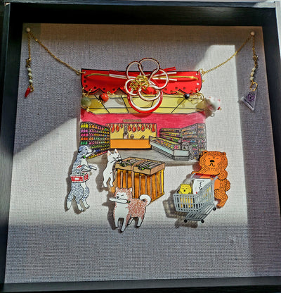 Shadowbox assembling of small sculptural pieces. Small dogs walk around a supermarket, pushing carts or holding baskets. Gold beads and strings decorate the piece.