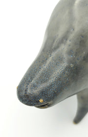 Gray ceramic sculpture of a rounded body quadruped creature with an open mouth goofy smile. It has tiny golden dot eyes blue speckled body.