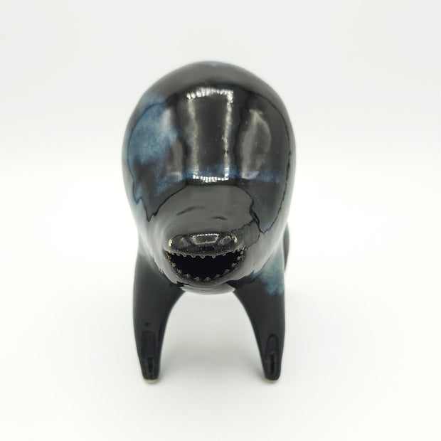 Black and blue ceramic sculpture of a rounded body quadruped creature with an open mouth goofy smile. It has tiny golden dot eyes and a galactic pattern body.