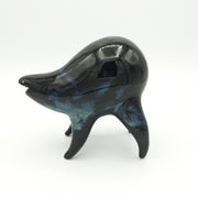 Black and blue ceramic sculpture of a rounded body quadruped creature with an open mouth goofy smile. It has tiny golden dot eyes and a galactic pattern body.