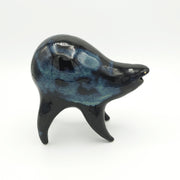 Black and blue ceramic sculpture of a rounded body quadruped creature with an open mouth goofy smile. It has tiny golden dot eyes and a galactic pattern body.