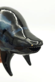 Black and blue ceramic sculpture of a rounded body quadruped creature with an open mouth goofy smile. It has tiny golden dot eyes and a galactic pattern body.