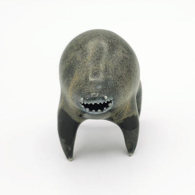Black and dark gray ceramic sculpture of a rounded body quadruped creature with an open mouth goofy smile. It has small silver eyes and a gritty texture on its body.