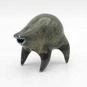 Black and dark gray ceramic sculpture of a rounded body quadruped creature with an open mouth goofy smile. It has small silver eyes and a gritty texture on its body.