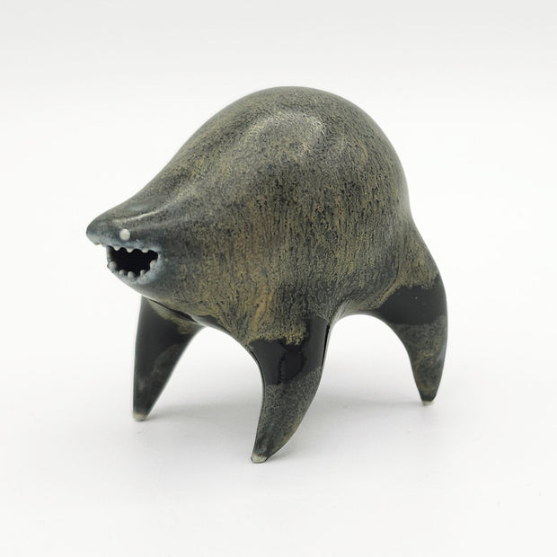 Black and dark gray ceramic sculpture of a rounded body quadruped creature with an open mouth goofy smile. It has small silver eyes and a gritty texture on its body.