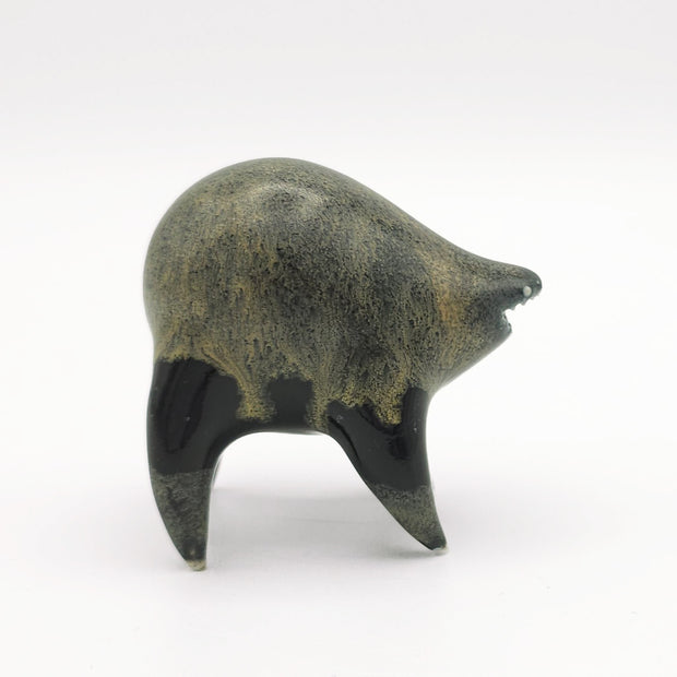 Black and dark gray ceramic sculpture of a rounded body quadruped creature with an open mouth goofy smile. It has small silver eyes and a gritty texture on its body.