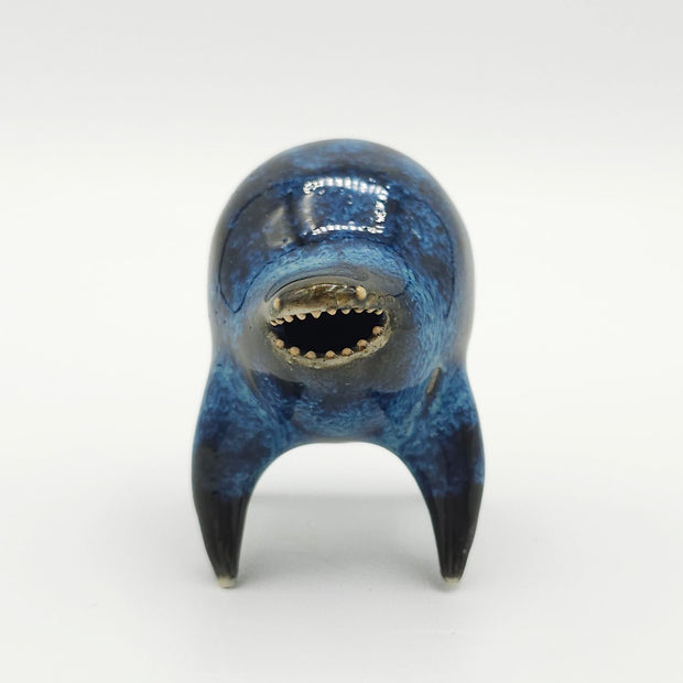 Black and blue ceramic sculpture of a rounded body quadruped creature with an open mouth goofy smile. It has small golden eyes and a swirling texture on its body.