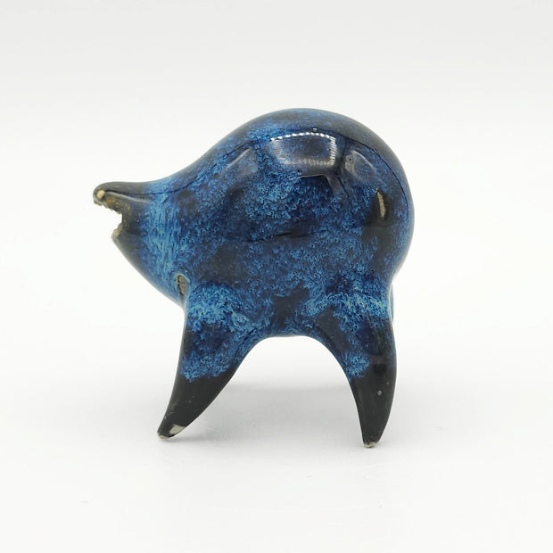 Black and blue ceramic sculpture of a rounded body quadruped creature with an open mouth goofy smile. It has small golden eyes and a swirling texture on its body.