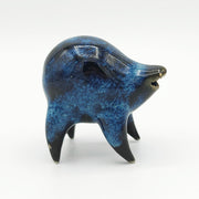 Black and blue ceramic sculpture of a rounded body quadruped creature with an open mouth goofy smile. It has small golden eyes and a swirling texture on its body.