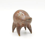 Orangish brown ceramic sculpture of a rounded body quadruped creature with an open mouth goofy smile. It has small golden eyes and an oil slick texture on its body.