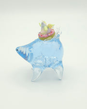 Resin sculpture of a blue rounded body quadruped creature with the illusion of water inside of its body. On its back is a pastel winged chubby creature in a donut shaped inflatable tube.