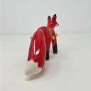 Ceramic sculpture of a red fox with a very fluffy tail, black paws, and has a simplistic drawn on face. Coming out from its body are small yellow flames.