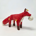 Ceramic sculpture of a red fox with a large fluffy tail and black paws. It holds a cap in its mouth, white and black with a Big Boss Robot logo on it. Small yellow flames come off of the fox's body.
