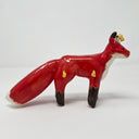 Ceramic sculpture of a red fox with a very fluffy tail, black paws, and has a simplistic drawn on face. Coming out from its body are small yellow flames.