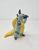 Ceramic sculpture of a kaiju style monster, standing on its hind legs with its arms situated out. It has a silver beak, mint colored body with a yellow belly, yellow fin on its back and a yellow dinosaur tail. It has silver spikes along its back and a red eye.