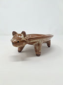 Ceramic plate or very shallow vessel, with a brown raccoon head in the front and 4 legs that act as stands for the vessel, attached. It has a fluffy, long tail.