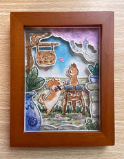 Framed shadow box style watercolor collage of a cute dog holding a flower in its mouth and jumping up on a stool where a surprised looking cat sits. They are on a patio like area with potted plants and signage.