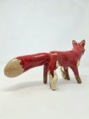 Glossy ceramic sculpture of a red fantasy style fox with a very fluffy tail and cream colored flames coming off its front paw and spreading slowly onto its body.