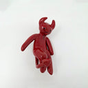 Glossy red ceramic sculpture of a devil with long limbs and curved head horns. It is mounted to the wall and has tears running down its face.