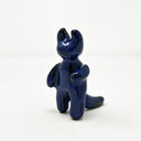 Dark blue ceramic sculpture of a figure with smooth limbs with little definition standing on 2 legs. It has 2 thick curved horns atop its head, like a devil