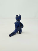 Dark blue ceramic sculpture of a figure with smooth limbs with little definition standing on 2 legs. It has 2 thick curved horns atop its head, like a devil