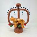 Glossy ceramic sculpture of a brown vessel with a thin center shape and 2 large handles. In front of it is a tiger with some lily pads and red flowers. Dark blue spheres come out of short wire along the top of the handles.